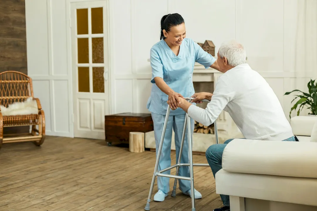 A caregiver steadying an older man as he stands with a walker