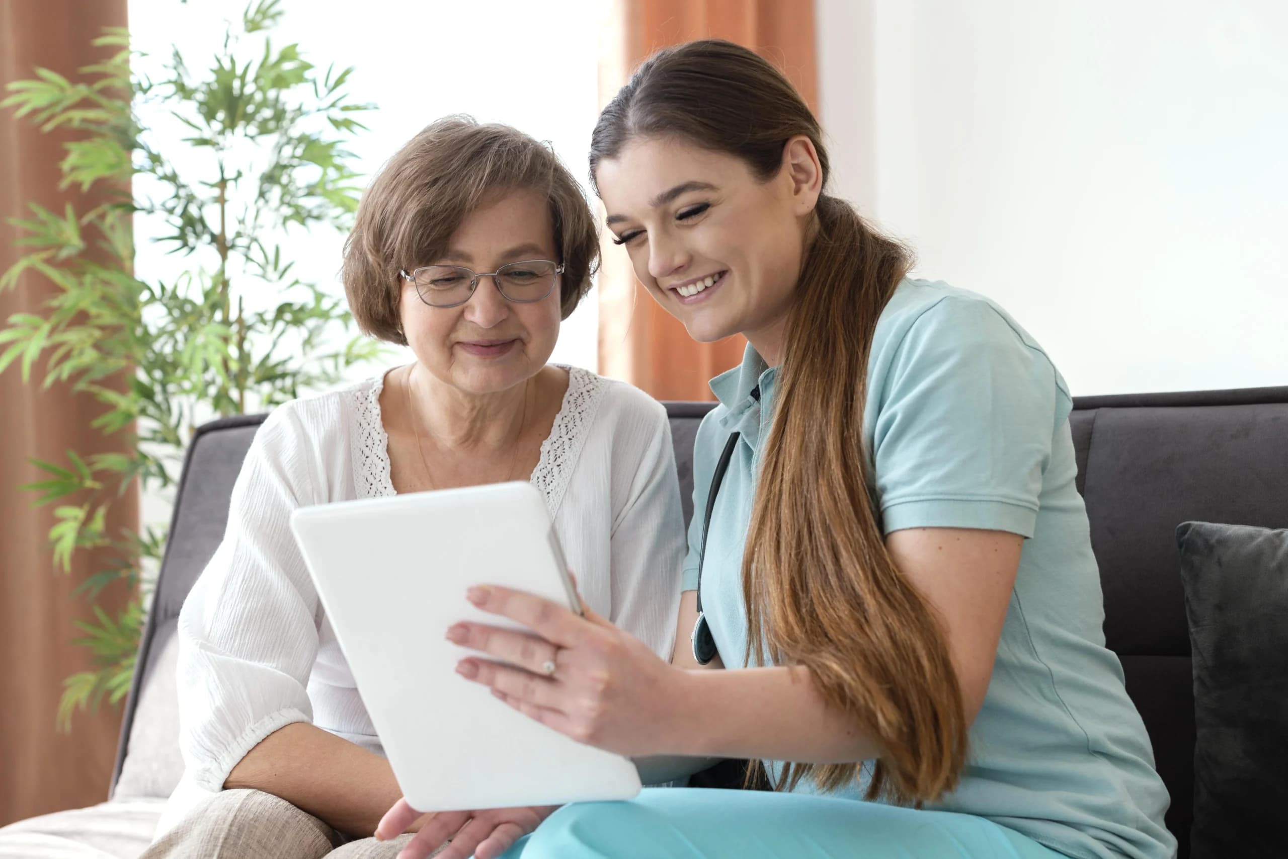 A caregiver showing an older woman something on a tablet