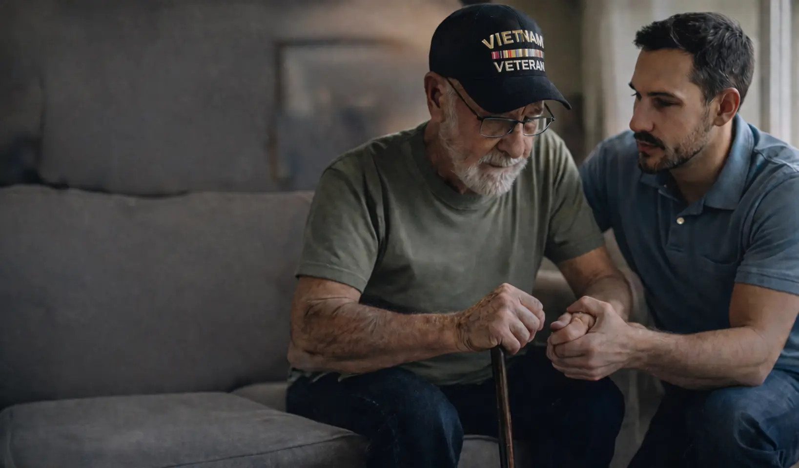A Vietnam veteran with a cane sitting on a sofa while a younger man holds his hand